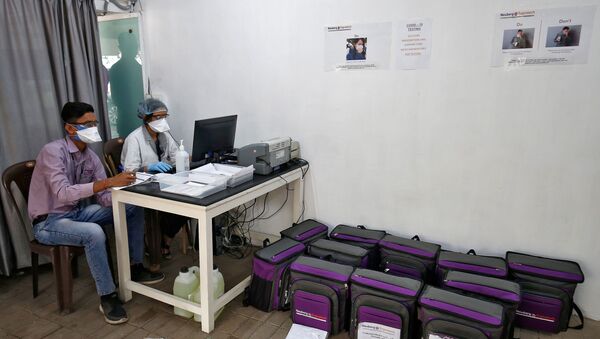 Laboratory technicians sit next to boxes containing coronavirus disease (COVID-19) testing kits at a sample collection centre in Ahmedabad, India March 26, 2020. - Sputnik International