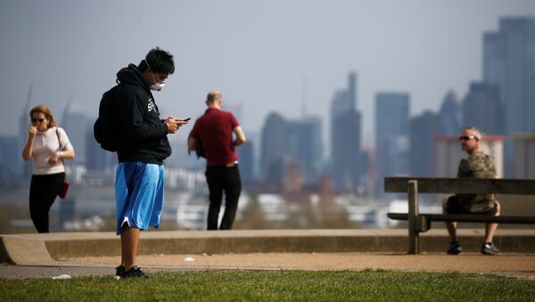 A man wearing a face mask looks at his phone on Primrose Hill in London - Sputnik International