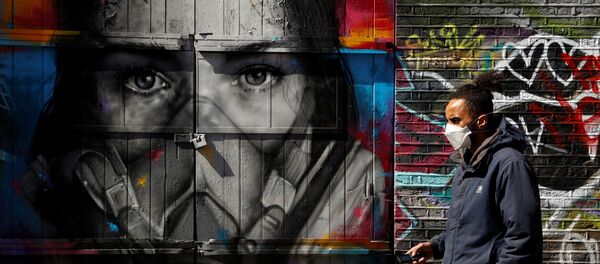 A man wearing a mask walks in Brick Lane in front of graffiti as the spread of the coronavirus disease (COVID-19) continues, London, Britain, April 14, 2020 - Sputnik International