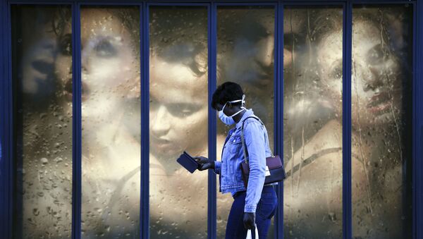 A woman wearing a protective mask walks past a store window in Paris  - Sputnik International