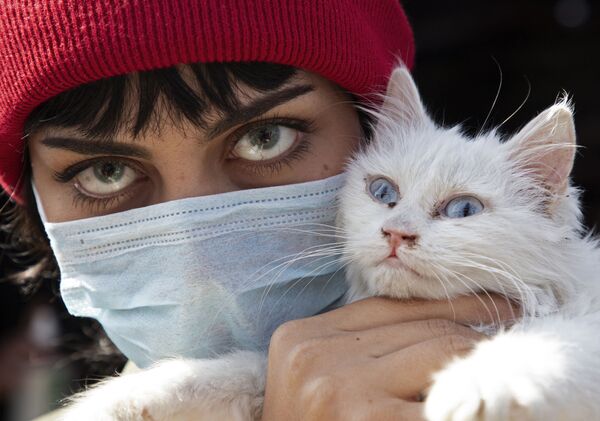 An Iraqi woman wearing a protective mask and coloured contact lenses holds her cat as she poses for a picture during a protest against corruption in the Iraqi government in the southern city of Basra in February 2020 - Sputnik International