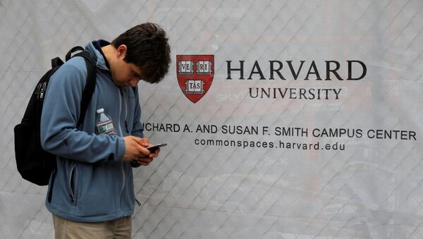 A man looks at his mobile phone beside a sign for Harvard University in Cambridge, Massachusetts, U.S., June 18, 2018. - Sputnik International