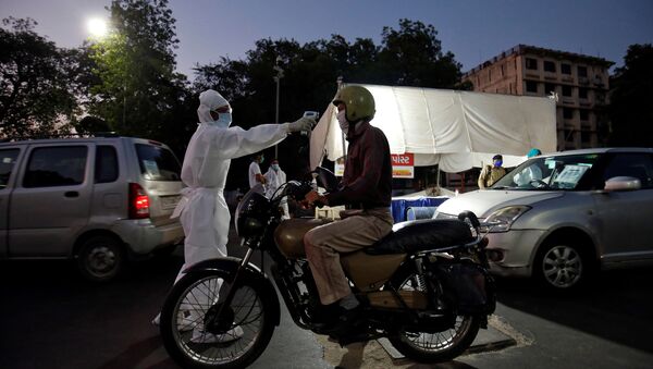 A health worker uses an infrared thermometer to measure the temperature of a motorcyclist on a road in India - Sputnik International