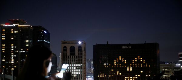 A woman wearing a protective face mask uses her phone as the Millennium Hilton Hotel lights up its rooms in the shape of a smiling emoji to comfort people amid the coronavirus disease (COVID-19) outbreak in Seoul, South Korea, April 26, 2020. - Sputnik International