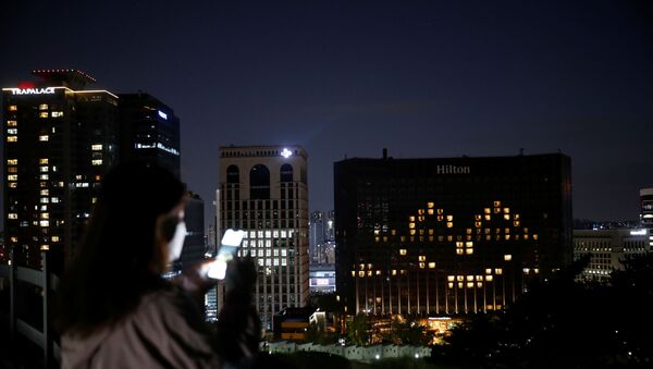 A woman wearing a protective face mask uses her phone as the Millennium Hilton Hotel lights up its rooms in the shape of a smiling emoji to comfort people amid the coronavirus disease (COVID-19) outbreak in Seoul, South Korea, April 26, 2020. - Sputnik International