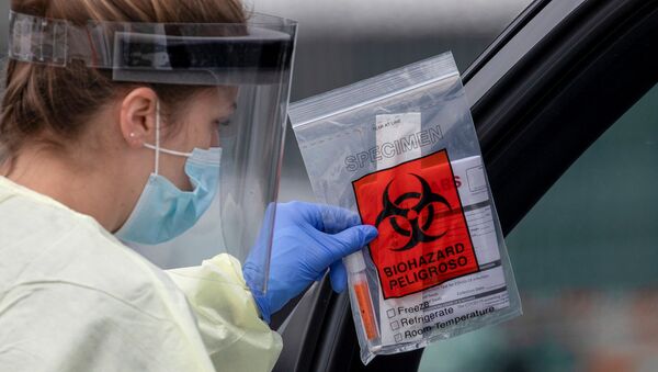 A health worker in protective gear hands out a self-testing kit in a parking lot of Rose Bowl Stadium during the global outbreak of the coronavirus disease (COVID-19), in Pasadena, California, U.S., April 8, 2020. - Sputnik International