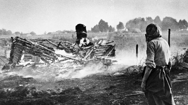 A woman stands next to a burnt house in a village during WW II - Sputnik International