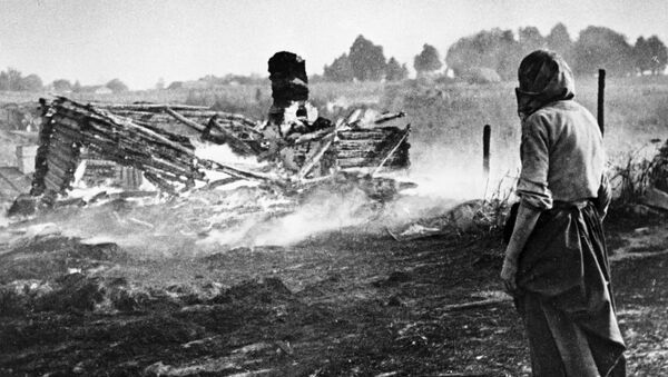 A woman stands next to a burnt house in a village during WW II - Sputnik International