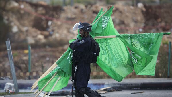 A member of the Israeli security forces carries flags of the Palestinian movement Hamas found at a clashing site near Ramallah, West Bank, Thursday, Oct. 8, 2015 - Sputnik International