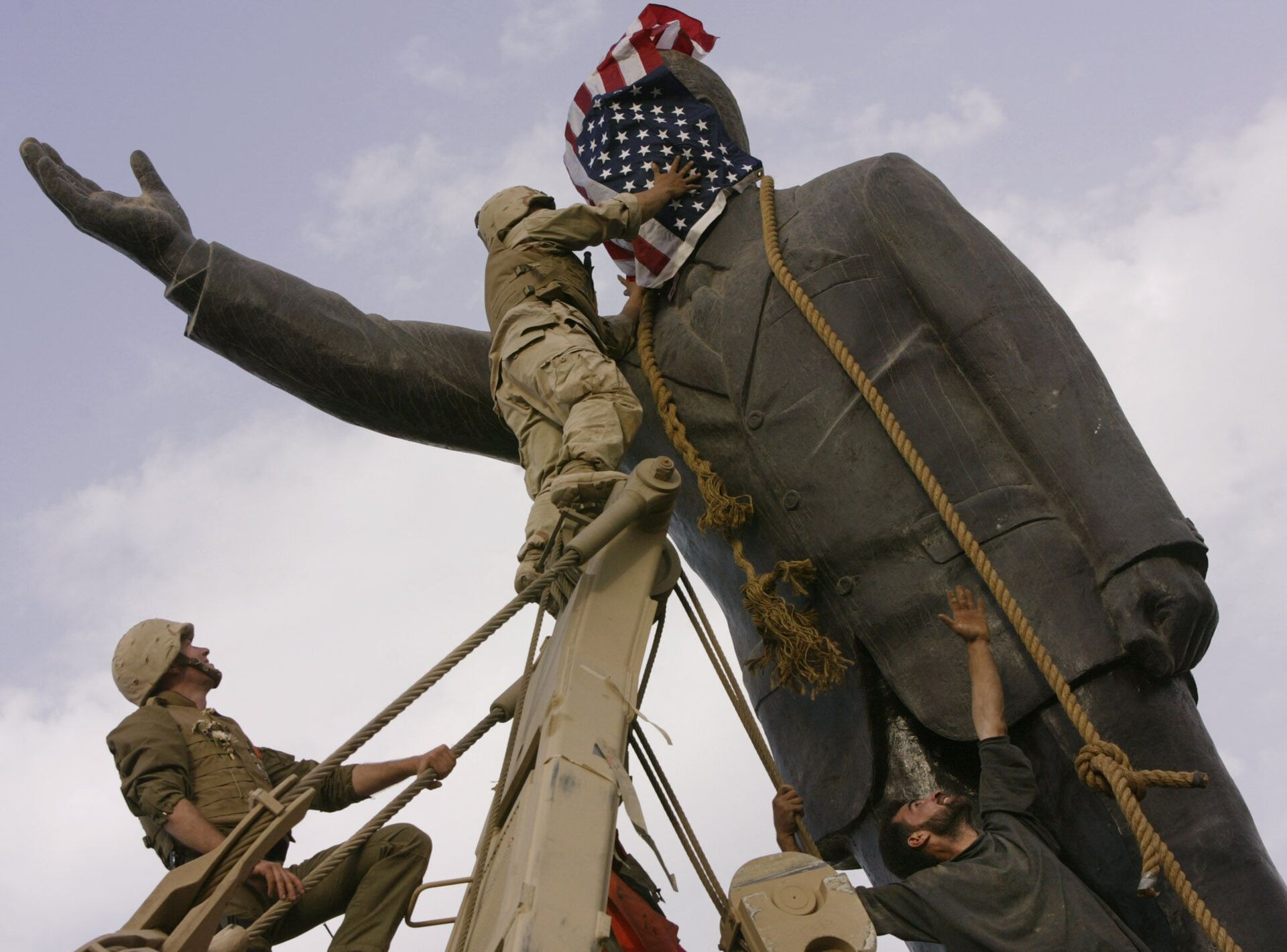 In this file photo taken Wednesday, April 9, 2003, an Iraqi man, bottom right, watches Cpl. Edward Chin of the 3rd Battalion, 4th Marines Regiment, cover the face of a statue of Saddam Hussein with an American flag before toppling the statue in downtown in Baghdad, Iraq. - Sputnik International, 1920, 30.12.2021