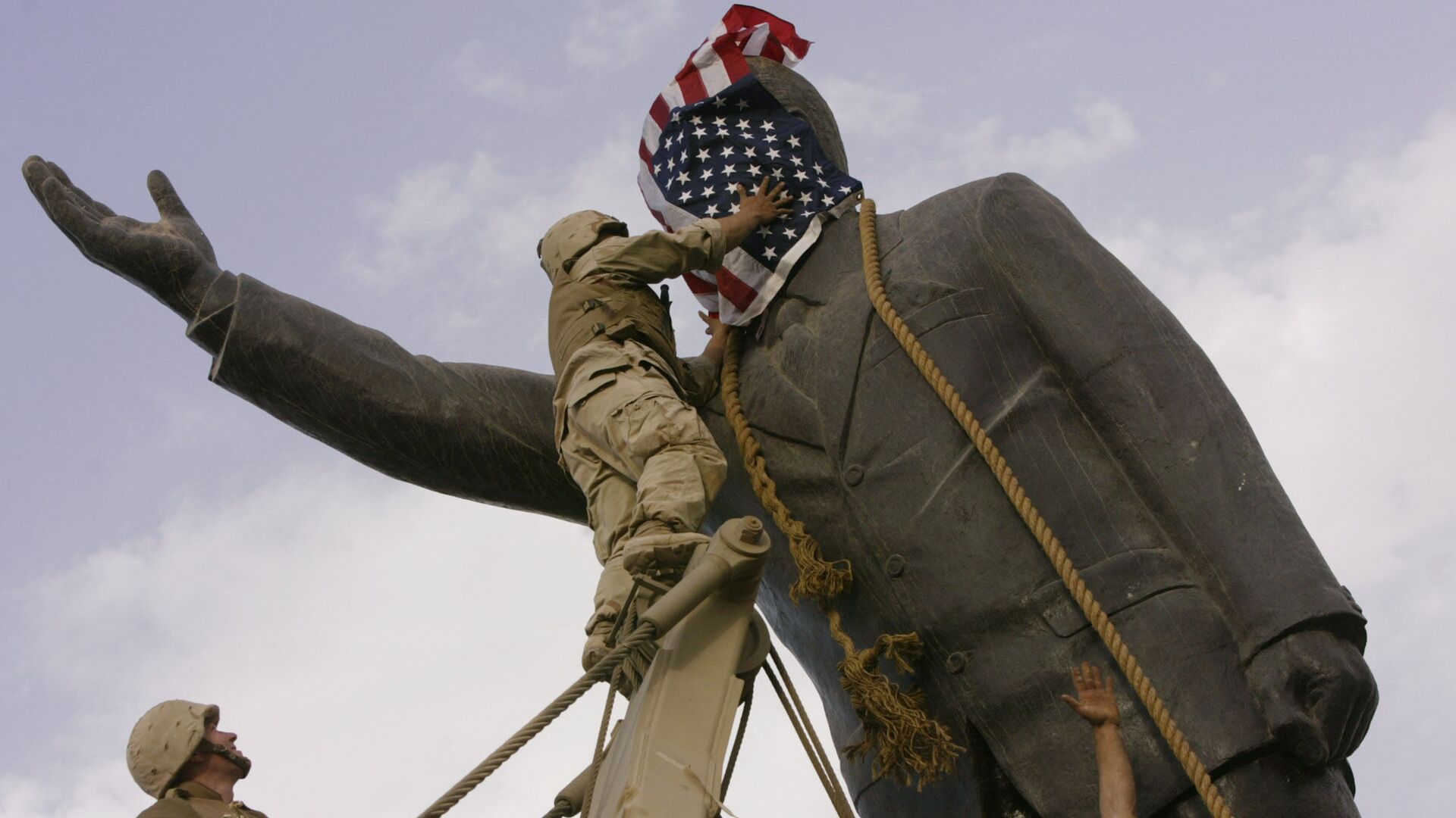 In this file photo taken Wednesday, April 9, 2003, an Iraqi man, bottom right, watches Cpl. Edward Chin of the 3rd Battalion, 4th Marines Regiment, cover the face of a statue of Saddam Hussein with an American flag before toppling the statue in downtown in Baghdad, Iraq. - Sputnik International, 1920, 26.03.2021
