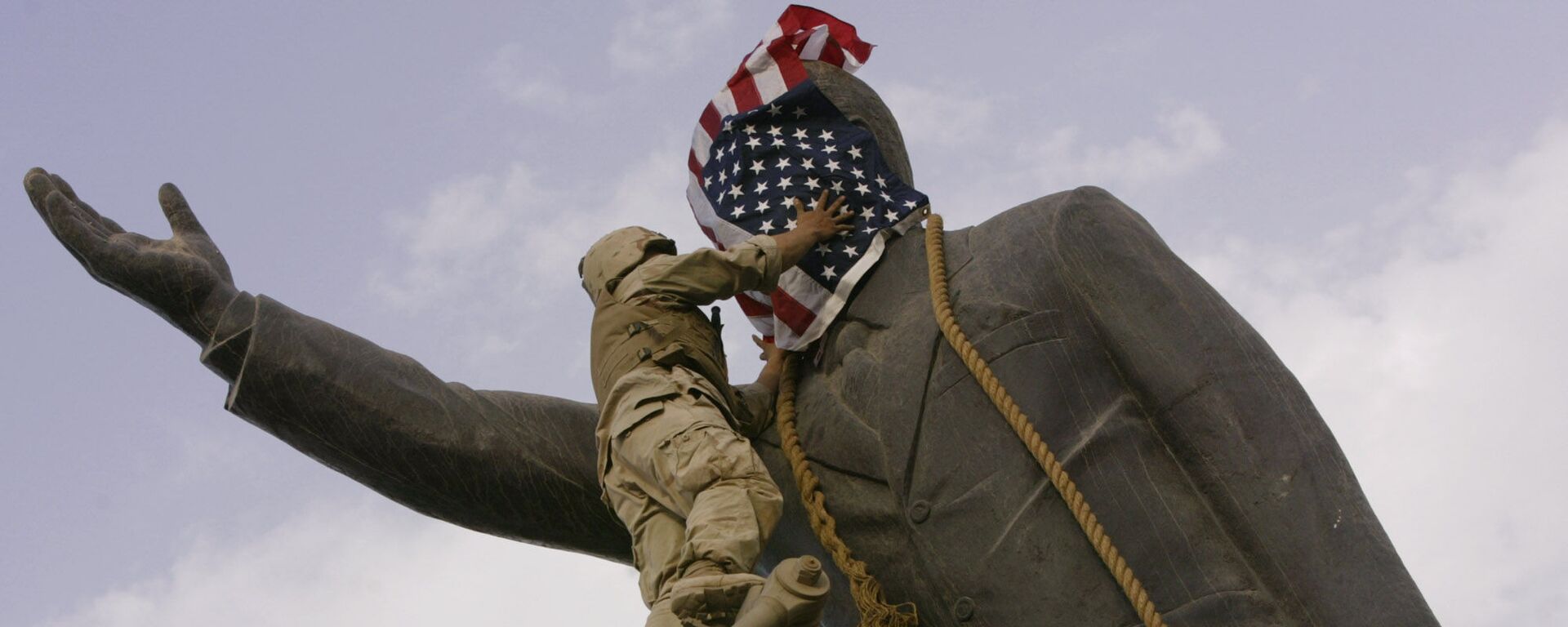 In this file photo taken Wednesday, April 9, 2003, an Iraqi man, bottom right, watches Cpl. Edward Chin of the 3rd Battalion, 4th Marines Regiment, cover the face of a statue of Saddam Hussein with an American flag before toppling the statue in downtown in Baghdad, Iraq. - Sputnik International, 1920, 17.03.2023