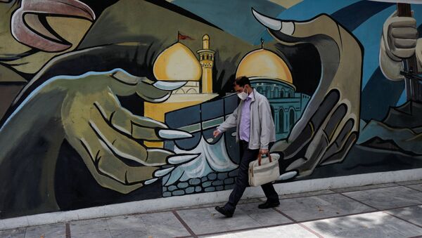 A man wearing a protective face mask walks past a Palestine mural in Tehran - Sputnik International