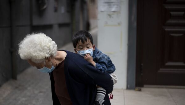 An elderly woman wearing a face mask piggybacks a boy along a street in  Beijing on May 11, 2020 - Sputnik International