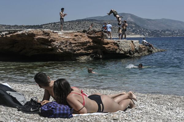 Sunbathers watch a young man doing a backflip into the water as they lie on the beach in Athen's southern suburb on 9 May 2020, as the nations readies for the reopening of schools and most of shops starting 11 May. - Sputnik International