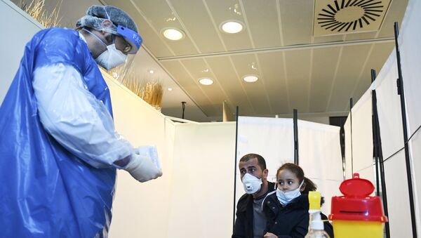 A medical staff member wearing protective facemask and suit, and a face-shield, prepares to collect from a man and his daughter at a COVID-19 testing centre set up in the European Parliament on May 12, 2020 - Sputnik International