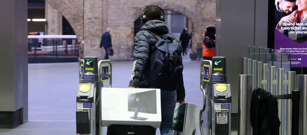 A man carries computer screens and equipment as he pulls a suitcase through the ticket barriers at King's Cross train station in central London, on March 19, 2020, as the coronavirus pandemic continues - Sputnik International