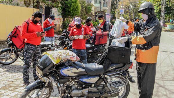 A Swiggy delivery man (R) wearing a facemask puts food commodities in the bag tied to his motorbike to deliver to customers as other Zomato delivery men check their mobile phones during a government-imposed nationwide lockdown as a preventive measure against the COVID-19 coronavirus, in Amritsar on March 28, 2020 - Sputnik International