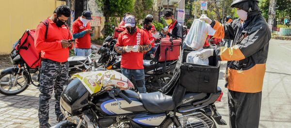 A Swiggy delivery man (R) wearing a facemask puts food commodities in the bag tied to his motorbike to deliver to customers as other Zomato delivery men check their mobile phones during a government-imposed nationwide lockdown as a preventive measure against the COVID-19 coronavirus, in Amritsar on March 28, 2020 - Sputnik International
