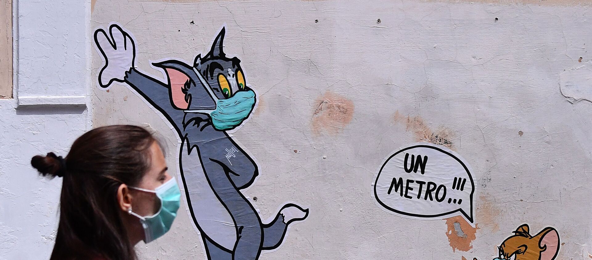 A woman wearing a face mask passes by a mural featuring William Hanna and Joseph Barbera' s characters Tom & Jerry mentioning the safe distance to be held from each other - One meter - in Rome, Friday, May 15, 2020 - Sputnik International, 1920