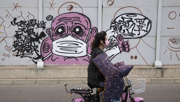 A woman wearing a mask against the coronavirus rides past graffiti with the words Wear your mask properly in Beijing on Friday, May 15, 2020. - Sputnik International
