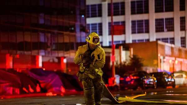 A firefighter drags a hose on San Pedro Street after a fire in a single-story commercial building sparked an explosion in the Toy District of downtown Los Angeles on May 16, 2020. - At least 11 firefighters were injured in downtown Los Angeles when a fire in a commercial building sparked a major explosion and spread to nearby structures, fire officials said. Some 230 responders battled the blaze as it spread to other buildings in the area before it was extinguished around two hours after it began. - Sputnik International