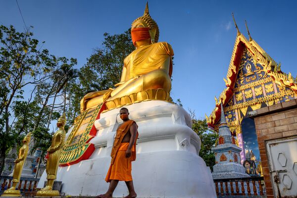 A monk walks in front of a giant Buddha statue wearing a face mask at Wat Nithet Rat Pradit temple in Pathum Thani outside Bangkok on 12 May 2020 - Sputnik International