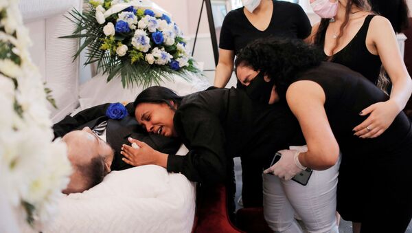 Maria Ortiz embraces the body of her partner Jose Holguin, 50, originally from the Dominican Republic and who died of complications related to the coronavirus disease (COVID-19), while she is supported by Mr. Holguin's family during his viewing service at International Funeral & Cremation Services in the Harlem neighborhood of Manhattan, New York City, U.S., May 16, 2020.  - Sputnik International