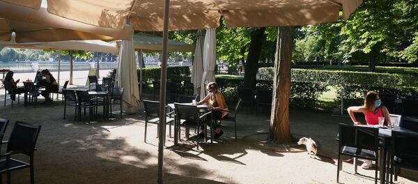 People wearing face masks sit at an outdoor seating section of a kiosk at Retiro Park as it is reopened for the first time in more than 2 months amid the coronavirus disease (COVID-19) outbreak, in Madrid, Spain May 25, 2020 - Sputnik International