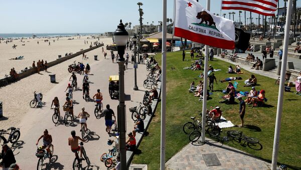 People sit at the beach as cyclists ride bicycles on Memorial Day weekend during the outbreak of the coronavirus disease (COVID-19) in Huntington Beach, California, U.S., May 23, 2020. - Sputnik International