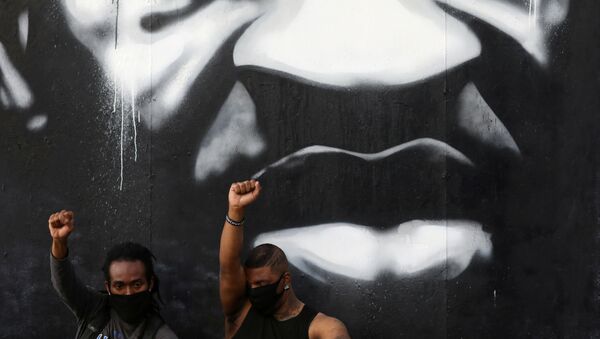 Two young men raise their fists as they sit in front of a mural of George Floyd - Sputnik International