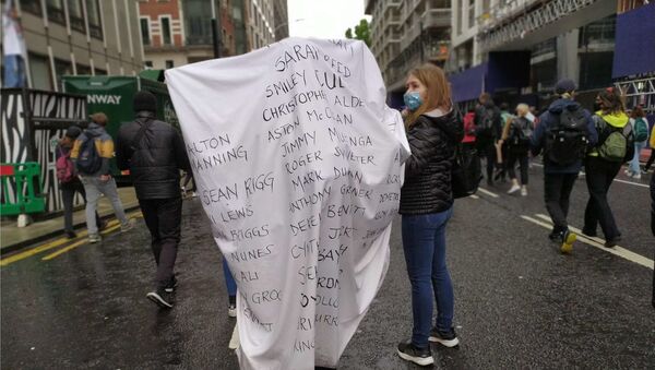 A woman walks down Victoria Street with the names of some of the people who have died in police custody in the UK over the last 10 years written on a sheet on her back.  - Sputnik International