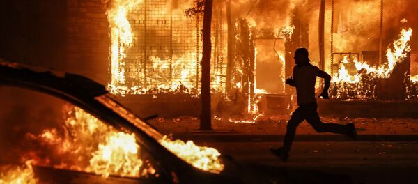 A protester runs past burning cars and buildings on Chicago Avenue, Saturday, May 30, 2020, in St. Paul, Minn. Protests continued following the death of George Floyd, who died after being restrained by Minneapolis police officers on Memorial Day. - Sputnik International