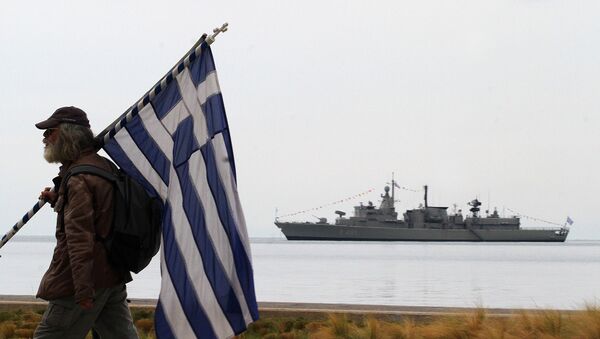 A spectator holds a Greek flag as a Greek Navy vessel is moored at Thermaikos Gulf during the annual military parade in the northern Greek port city of Thessaloniki on Tuesday, Oct. 28, 2014 - Sputnik International