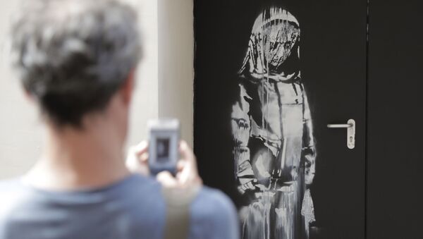 (FILES) In this file photo taken on June 25, 2018 a man takes a photograph of an artwork by street artist Banksy in Paris on a side street to the Bataclan concert hall where a terrorist attack killed 90 people on Novembre 13, 2015 - Sputnik International