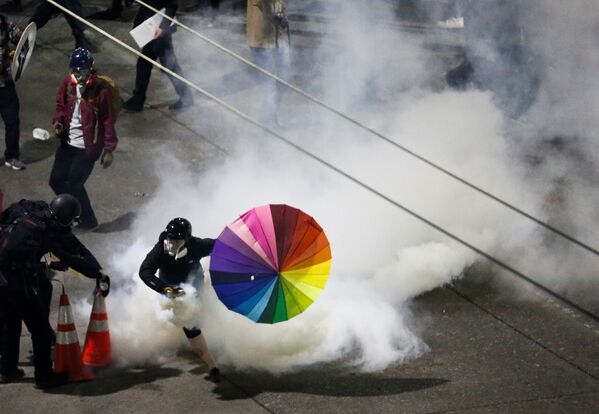 A protester with a rainbow umbrella picks up a gas canister as law enforcement deploys chemical agents and blast balls during a protest against racial inequality in the aftermath of the death in Minneapolis police custody of George Floyd, near the Seattle Police department's East Precinct in Seattle, Washington, U.S. June 8, 2020.  - Sputnik International