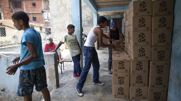 Residents help to unload and stack boxes of basic food staples, such as pasta, sugar and flour, provided by a government food assistance program, in Caracas’ slum of Petare, Venezuela, Thursday, April 30, 2020.  - Sputnik International