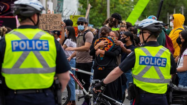 Two women hug in front of police as protesters march to highlight the deaths in the U.S. of Ahmaud Arbery, Breonna Taylor and George Floyd, and of Toronto's Regis Korchinski-Paquet, who died after falling from an apartment building while police officers were present, in Toronto, Ontario, Canada May 30, 2020.  - Sputnik International