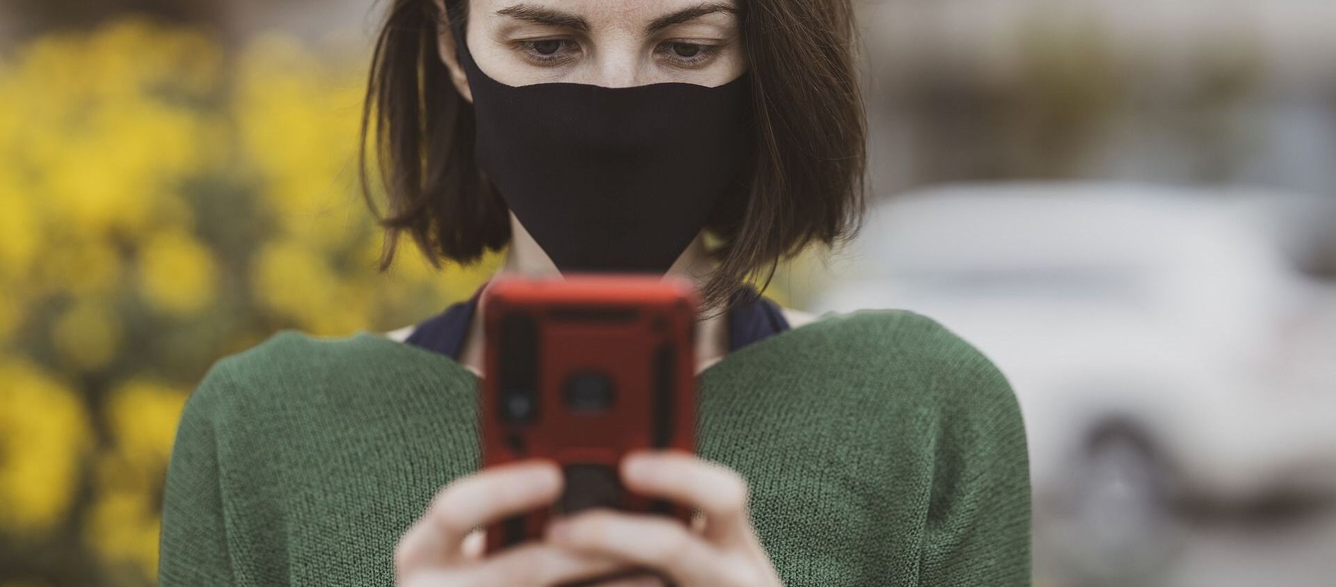 A woman wearing a face mask holds up her mobile phone - Sputnik International, 1920