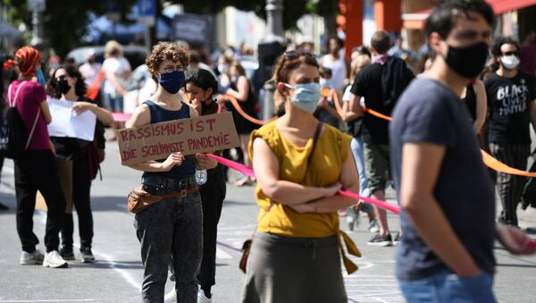 A person holds a banner reading Racism is the worst pandemic as participants of the so-called Indivisible demonstration form a human chain in support of the Black Lives Matter movement and to protest against the lockdown following the coronavirus disease (COVID-19) outbreak, in Berlin, Germany, June 14, 2020.  - Sputnik International