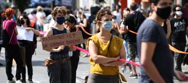 A person holds a banner reading Racism is the worst pandemic as participants of the so-called Indivisible demonstration form a human chain in support of the Black Lives Matter movement and to protest against the lockdown following the coronavirus disease (COVID-19) outbreak, in Berlin, Germany, June 14, 2020.  - Sputnik International