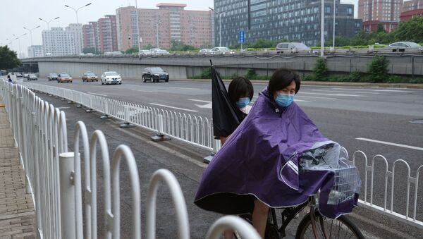 A woman wearing a raincoat and face mask amid rainfall in Beijing - Sputnik International