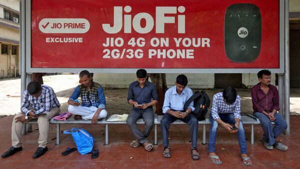 Commuters use their mobile phones as they wait at a bus stop with an advertisement of Reliance Industries' Jio telecoms unit, in Mumbai, India July 10, 2017 - Sputnik International