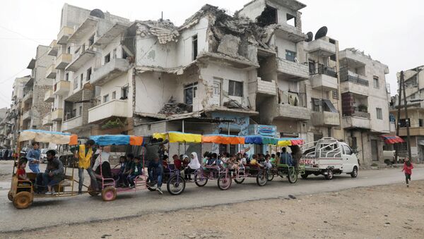 Children ride in carts past a damaged building on the first day of the Muslim holiday of Eid al-Fitr, amid the global outbreak of the coronavirus disease (COVID-19), in the opposition-held Idlib city in northwest Syria, May 24, 2020. - Sputnik International