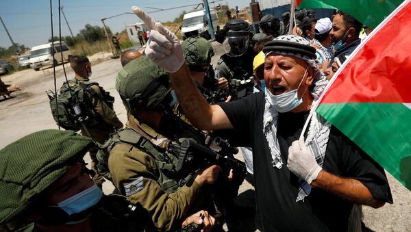FILE PHOTO: A demonstrator holding a Palestinian flag gestures in front of Israeli forces during a protest against Israel's plan to annex parts of the occupied West Bank, in Haris June 26, 2020. - Sputnik International