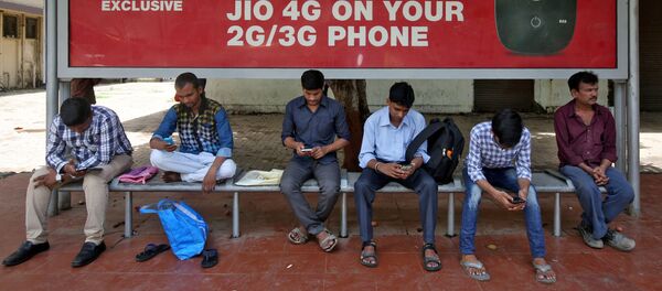 Commuters use their mobile phones as they wait at a bus stop with an advertisement of Reliance Industries' Jio telecoms unit, in Mumbai - Sputnik International