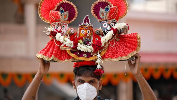 A Hindu devotee, wearing a protective face mask, carries idols of Hindu Lord Jagannath, his sister Subadhra and brother Balabhadra, as he arrives to attend the annual Rath Yatra - Sputnik International