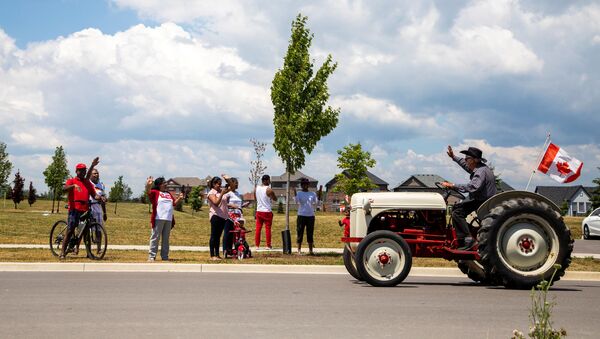 People watch from the sidewalk as a drive-by parade makes its away around town, during Canada Day celebrations in Newcastle, Ontario, Canada July 1, 2020. - Sputnik International