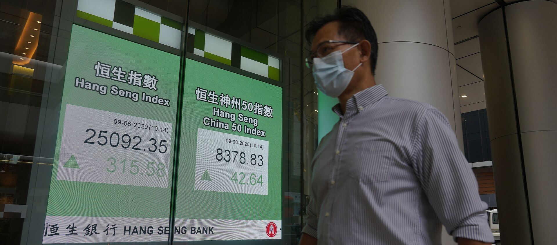 A man wearing a face mask walks past a bank electronic board showing the Hong Kong share index at Hong Kong Stock Exchange Tuesday, June 9, 2020. - Sputnik International, 1920