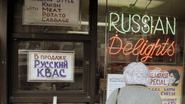 A Russian émigré stands outside a store in New York's Brighton Beach. The sign reads 'Russian kvas for sale.' - Sputnik International